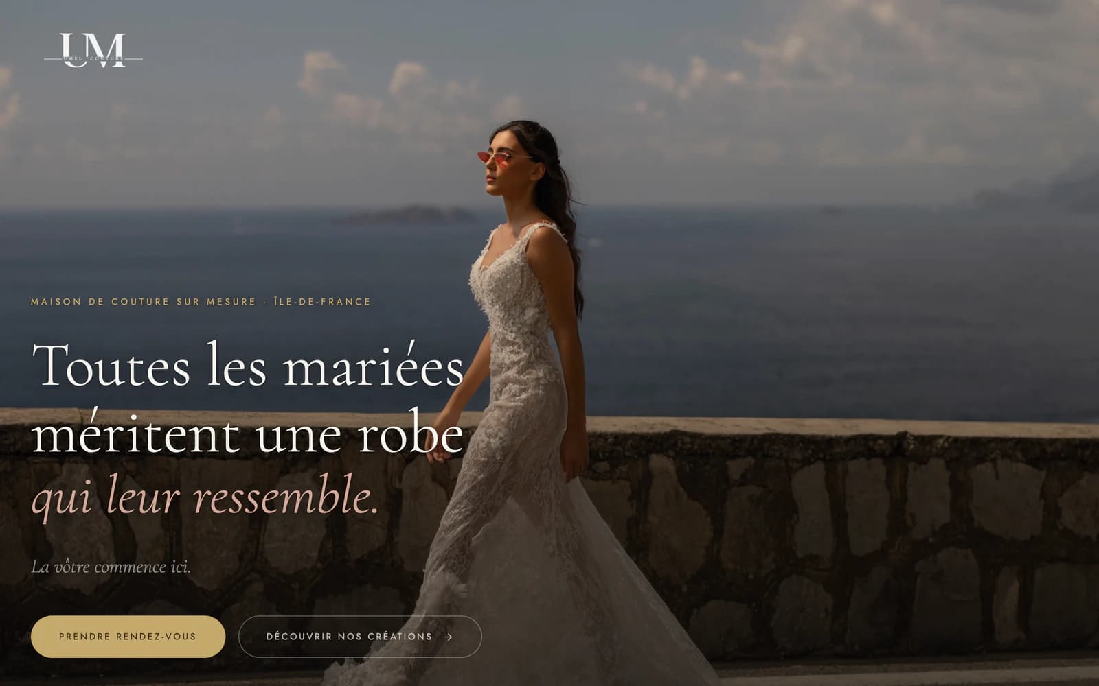 Page d’accueil d’Umel Couture : une mariée en robe de dentelle marche au bord de la mer